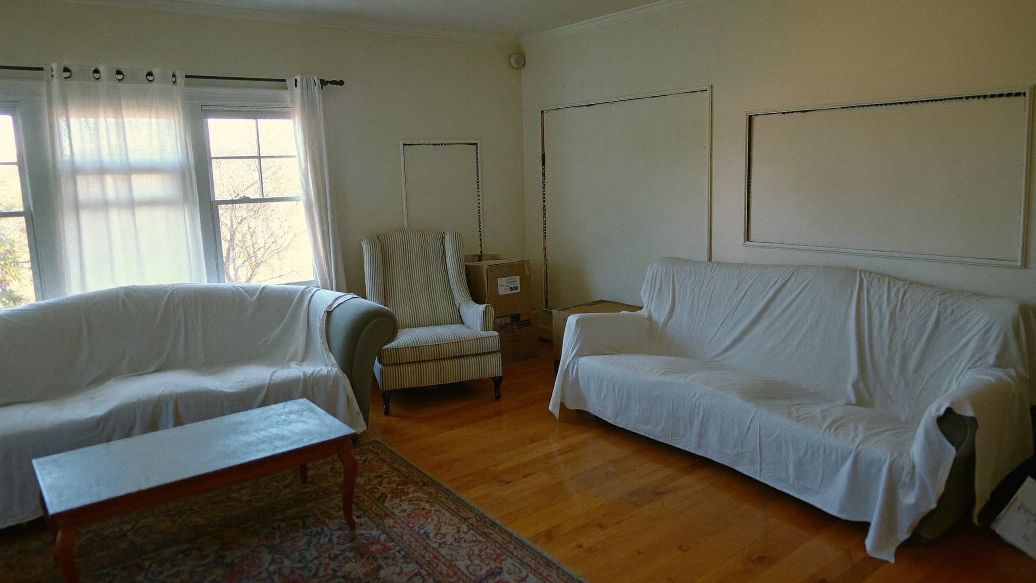 Living room of a recently inherited 1960s Bay Area home with furniture under white dust sheets and partially packed moving boxes — a house being settled after a death