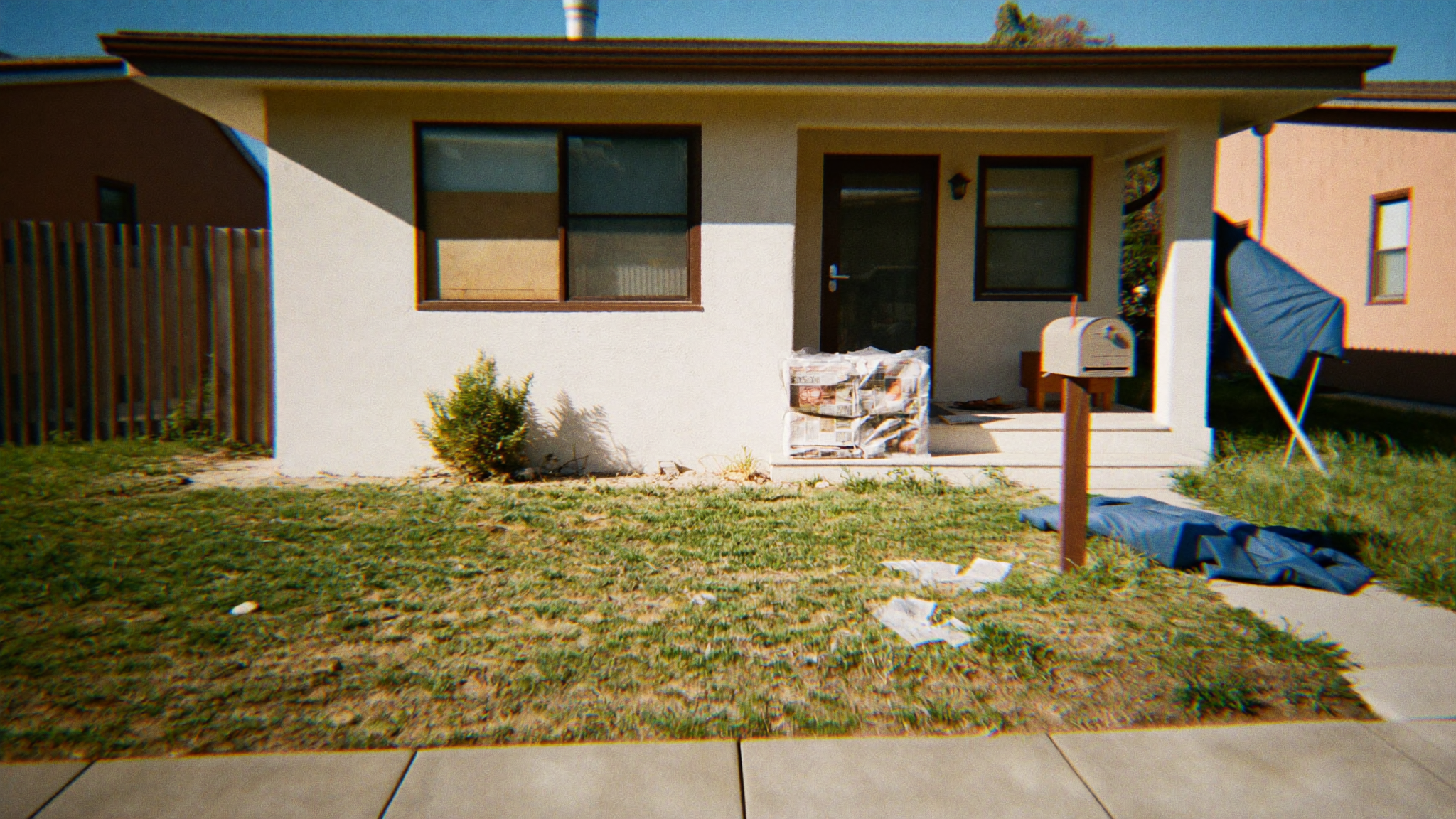 Small Bay Area stucco bungalow with overgrown lawn, accumulated mail, debris on the porch, and a blue tarp — classic exterior signs of a vacant or squatter-occupied property in East Oakland